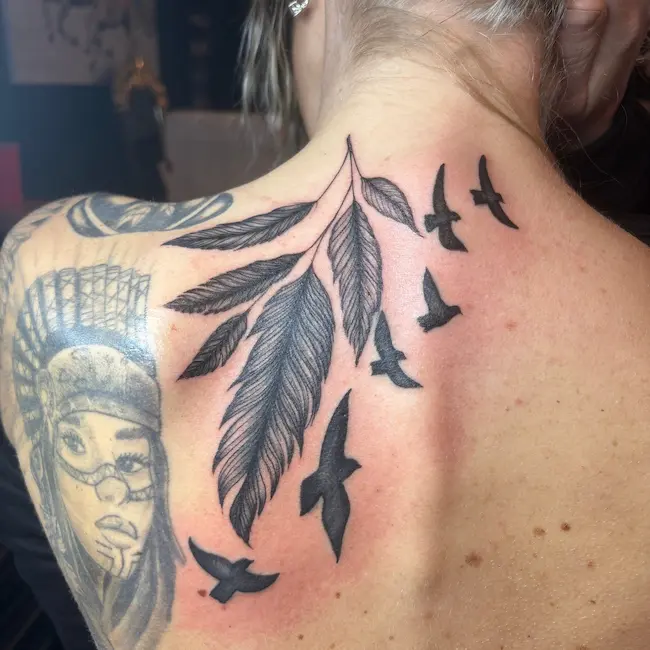 Birds flying underneath collection of feathers, blackwork back tattoo